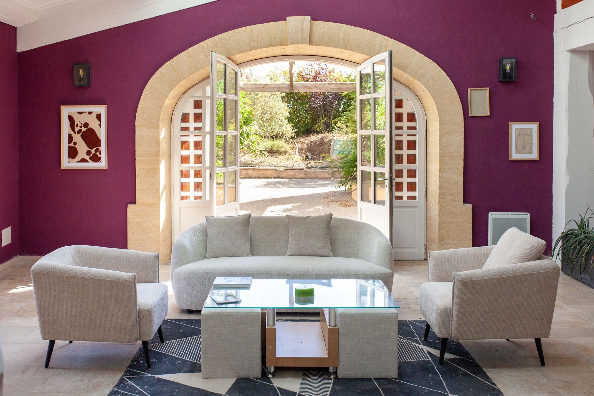 Salon aux murs violets du domaine, canapé crème et portes ouvertes sur le jardin