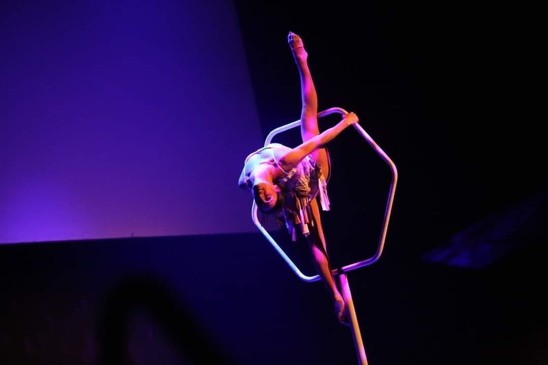 Artiste aérienne en représentation dans un cerceau, éclairée de violet et d’or