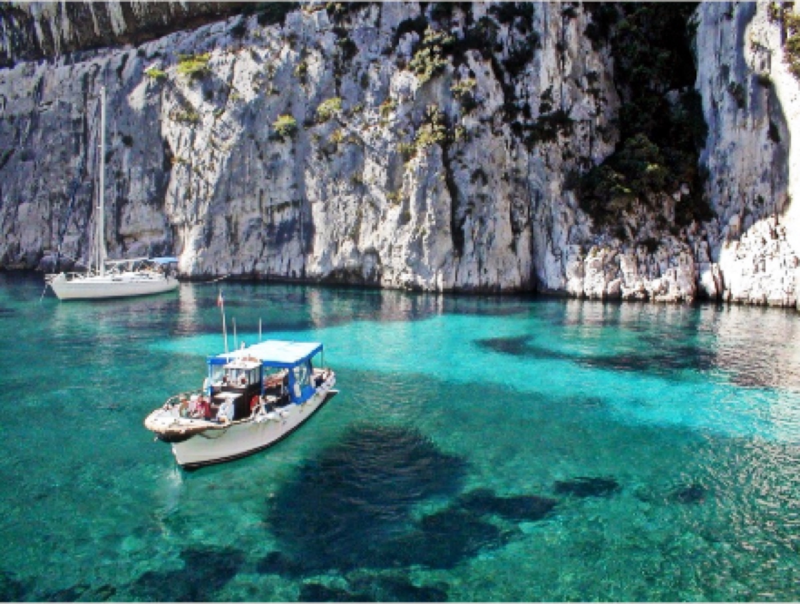 Bateau de promenade et voilier sur une eau turquoise au pied des falaises des Calanques de Marseille