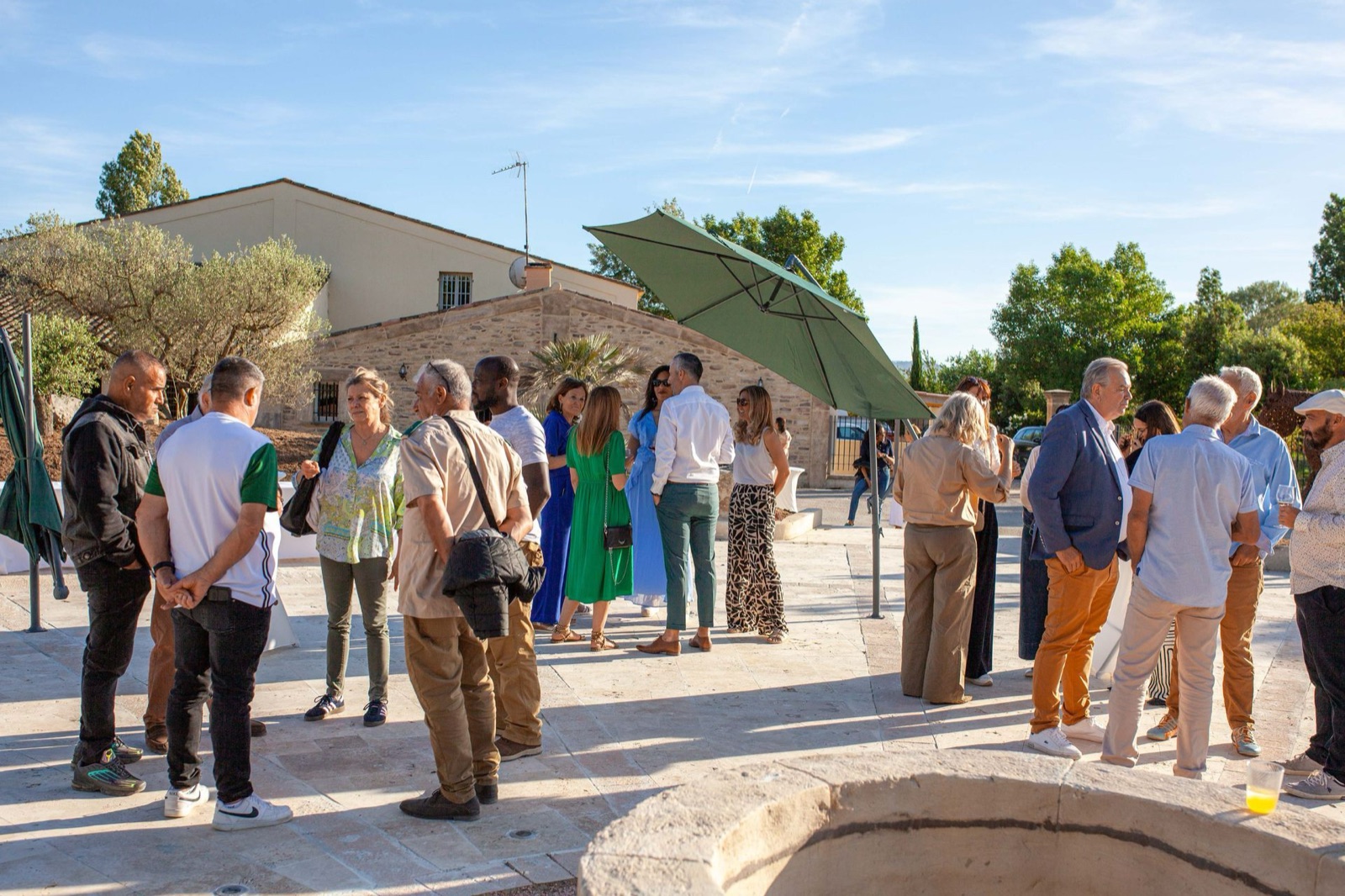 Invités réunis en extérieur près d’un bâtiment en pierre du domaine, sous les parasols