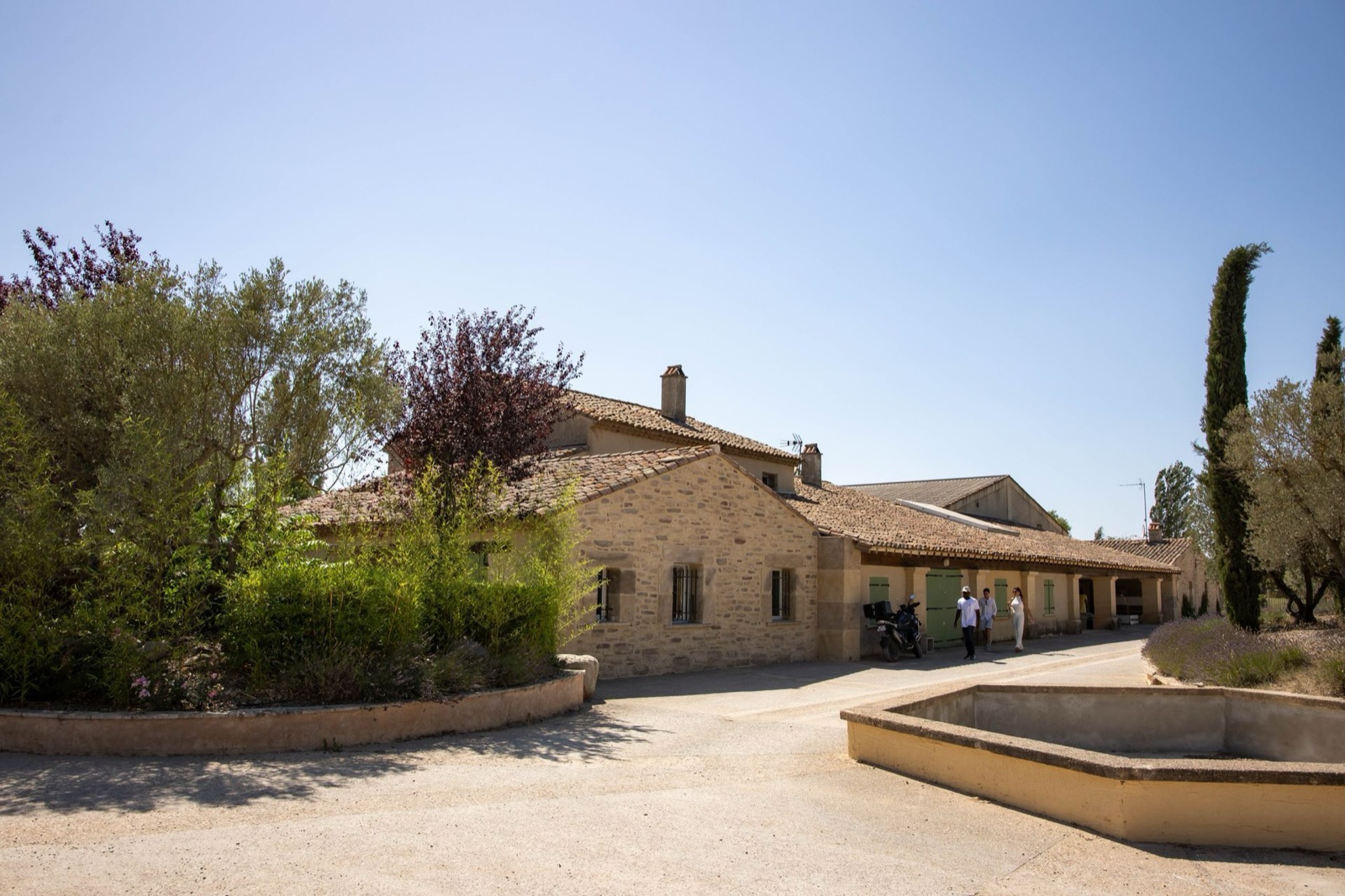 Bâtiment en pierre au toit de tuiles et fontaine, entourés d’arbres, au Domaine de la Myrtille