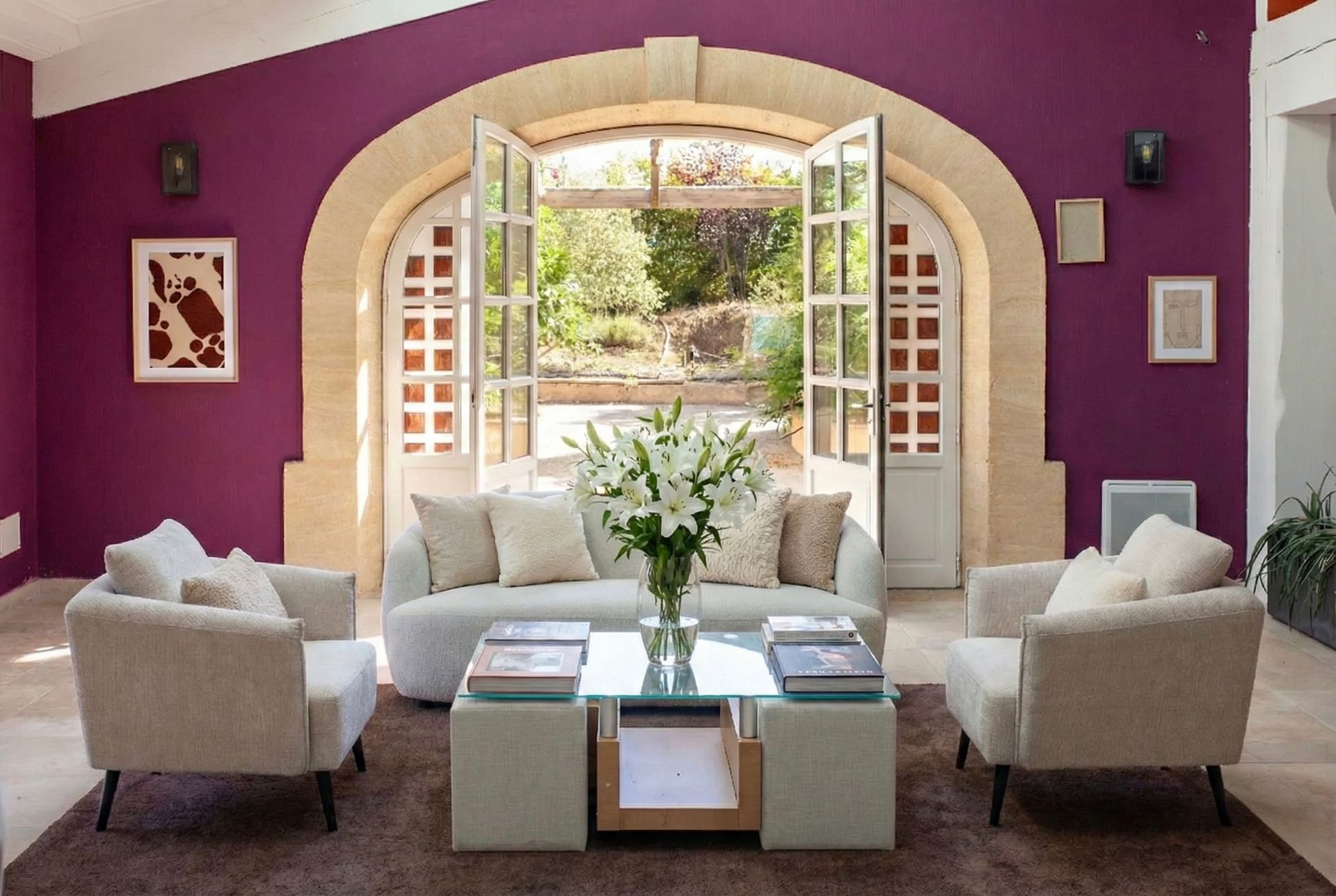 Salon avec murs violets, canapé crème, deux fauteuils et portes ouvertes sur un jardin.