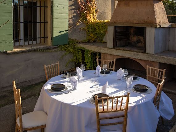 Terrasse privative d’un appartement du domaine, table en béton, chaises tressées et barbecue en pierre