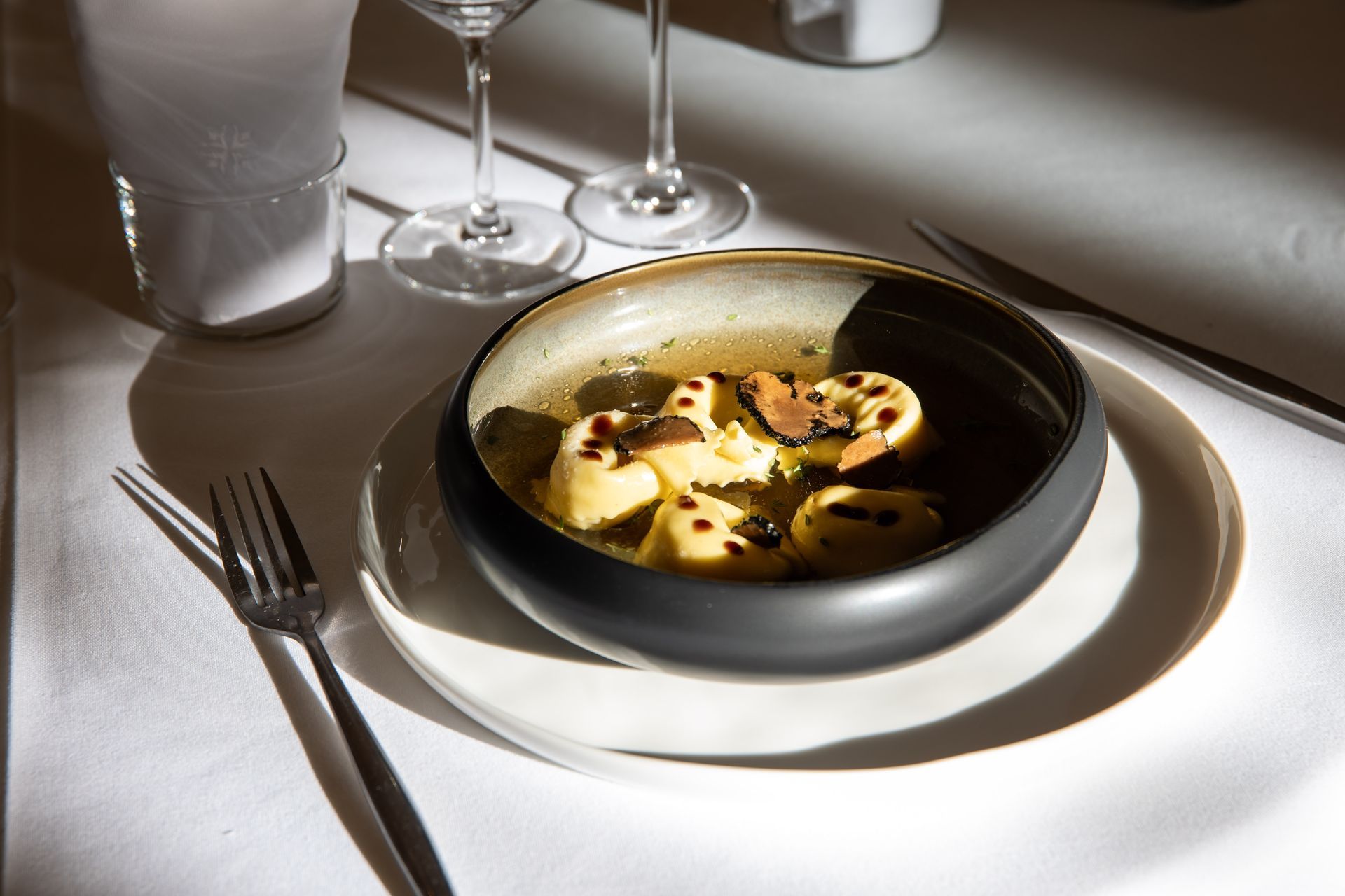 Bol de pâtes au bouillon, garni de truffes noires, sur une assiette blanche, dressage de table.