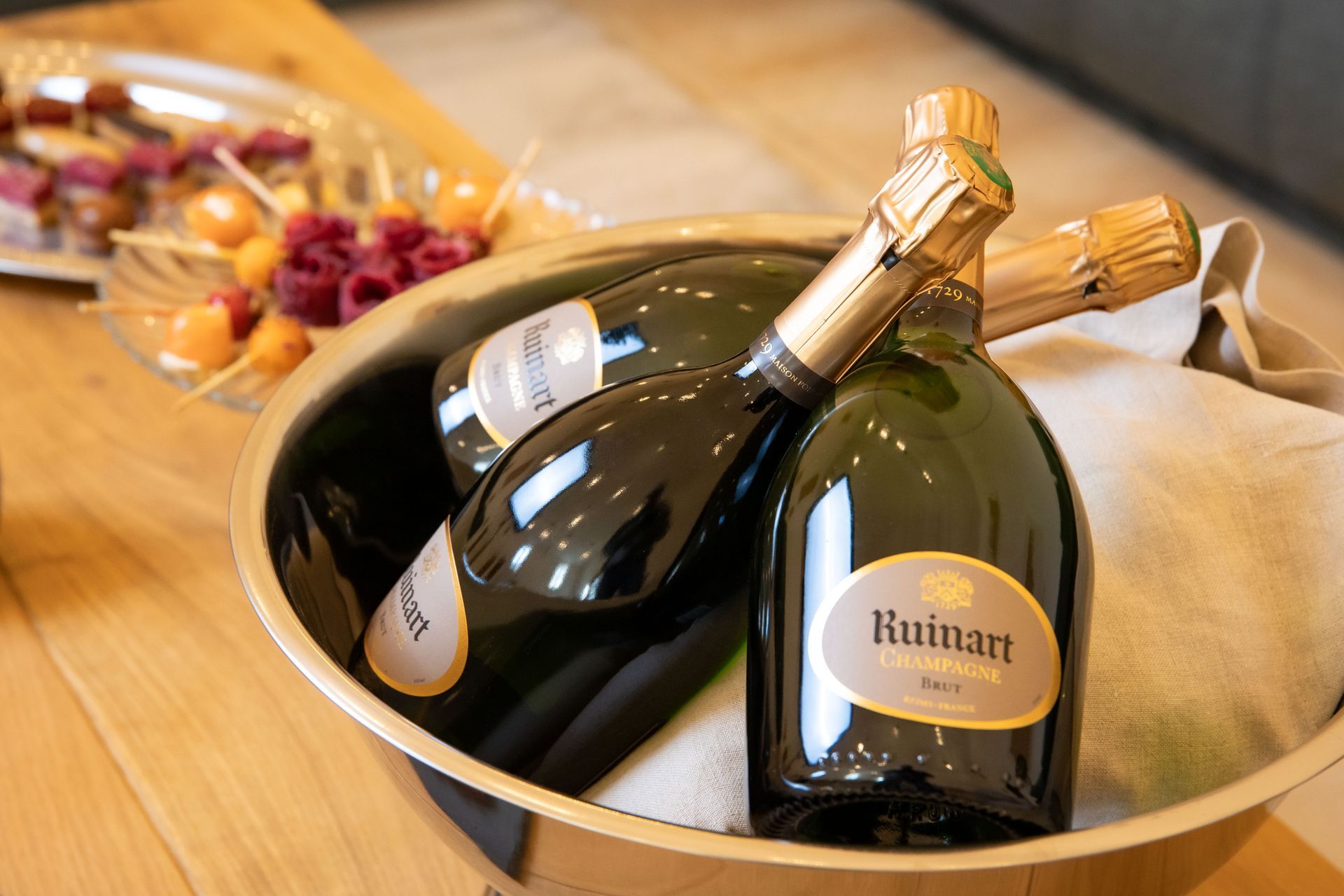 Trois bouteilles de champagne dans un seau doré avec des collations sur une assiette en arrière-plan.
